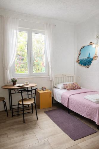 a bedroom with a bed and a table and two windows at Private Guest Room with Garden Access in Skopje
