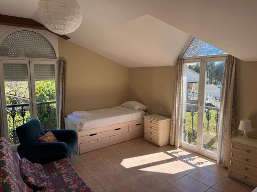 a bedroom with a bed and a chair and windows at La Zinca in Cambre