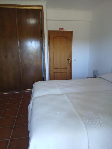 a bedroom with a white bed and a wooden door at Casa FIGUEIRAS in Bensafrim
