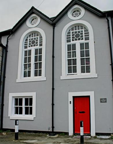 a white building with a red door and two windows at The Old Court House & Jail in Menai Bridge