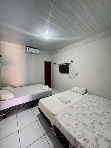 two beds in a room with a tv on the wall at Pousada e Chalés mar e sol in Manibu