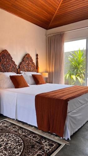 a bedroom with a bed with white sheets and a window at Alma Iguassu I Chalés com Banheira & Jardins in Foz do Iguaçu