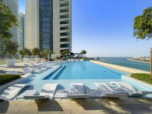 a swimming pool with white lounge chairs next to the ocean at Luxury 2 Bedroom Apartment - Private Beach - Emaar Beach Vista in Dubai