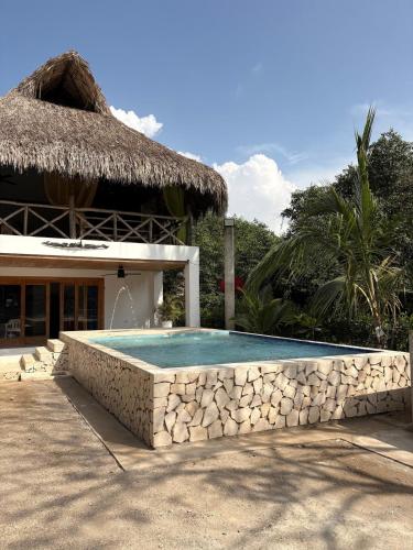 a swimming pool in front of a house with a thatch roof at Cabaña CasaMar Angelica in El Puertón