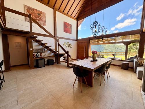 a dining room with a wooden table and a large window at Casa 04 Monte Boa Vista - Conforto com Piscina Privativa, Sauna e Lareira in Teresópolis