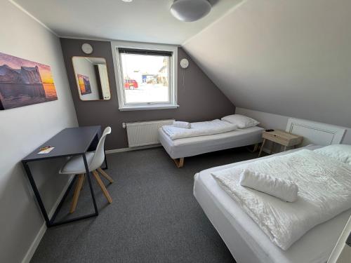 a small room with two beds and a desk and a window at Møller Guesthouse in Ilulissat