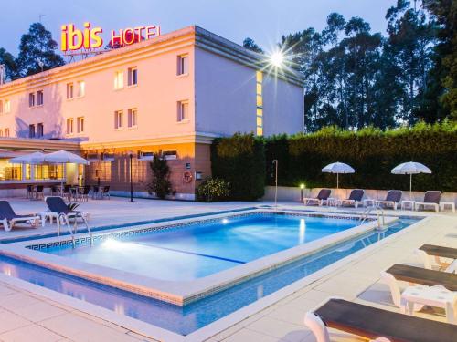 a pool in front of a hotel with chairs and umbrellas at Hotel ibis Porto Sul Europarque in Santa Maria Da Feira