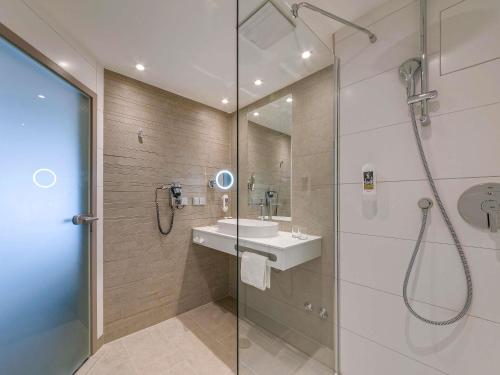 a bathroom with a shower and a sink and a mirror at Mercure Hotel am Entenfang Hannover in Hannover