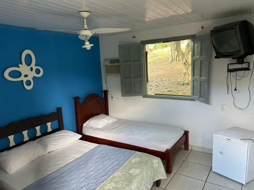 two beds in a room with a tv and a window at Pousada do pc in Bom Jesus do Itabapoana
