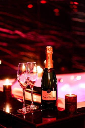 a bottle of wine and two glasses on a table at 007 Loveroom Secrète Jacuzzi privé Cinéma 4K in Courcouronnes