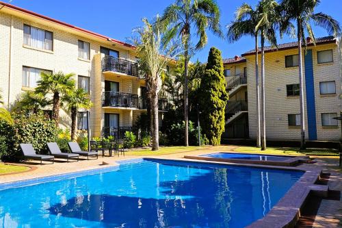 a swimming pool in front of a building with palm trees at Great Eastern Motor Lodge in Perth