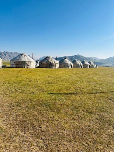 a field with a group of huts in the distance at NOMAD KEL-SUU Yurt Camp in Kol-Suu