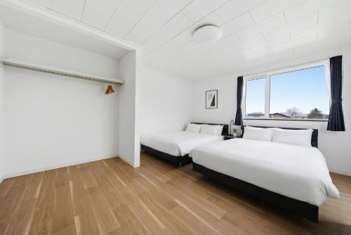 two beds in a room with white walls and wood floors at Nord Birch in Tōbetsu