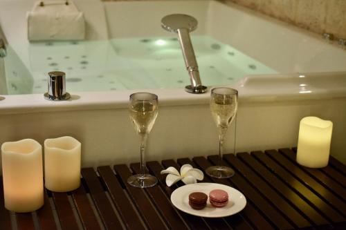 two glasses of wine and a plate of food in front of a bath tub at Le Trophée Boutique Hôtel Spa- La Loggia Appart'hôtel in Deauville
