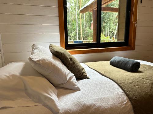 a bed with pillows and a window in a room at Cabañas Alto del Bosque in Coñaripe