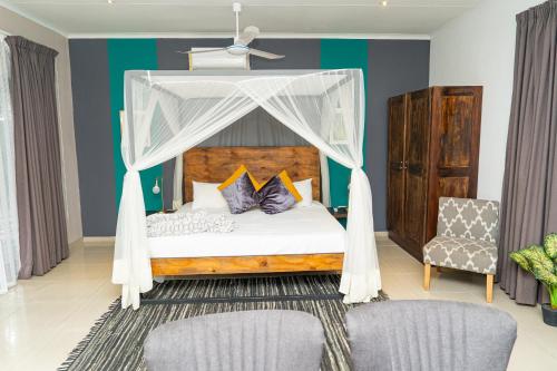 a bedroom with a canopy bed with two chairs at Cu Guest House in Phalaborwa