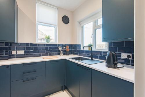 a blue and white kitchen with a sink and two windows at Folkestone Apartments in Folkestone