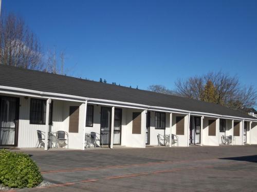 un edificio blanco con sillas en un aparcamiento en Rosetown Motel en Te Awamutu