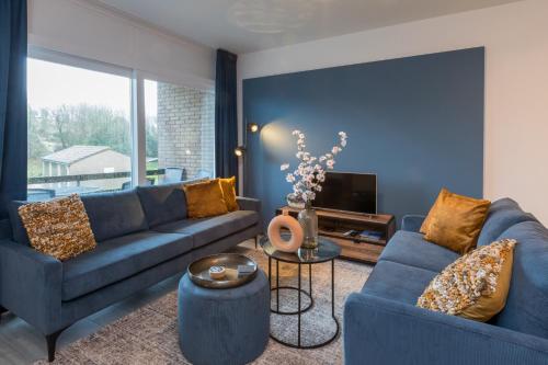 a living room with two blue couches and a tv at Welcome in - Appartement aan de duinen met balkon I Duinweg 18, Zoutelande 'Duinroos' in Zoutelande