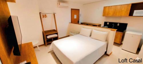 a small room with a white bed and a kitchen at Starlis Home - Versátil in Cuiabá