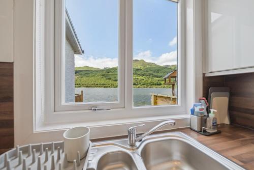 a kitchen sink with a window above it with a view of a lake at Cottage on the Loch in Arrochar