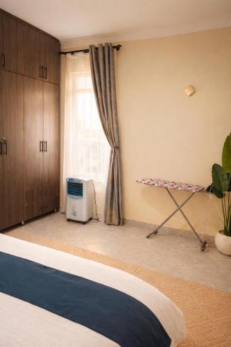 a bedroom with a bed and a table and a window at Cozy Apartment in Munyonyo in Munyonyo