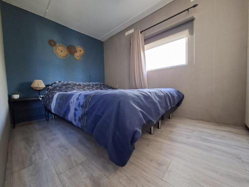 a bedroom with a bed with a blue comforter and a window at Gezellige, knusse, Stacaravan Banjer in Schoonloo