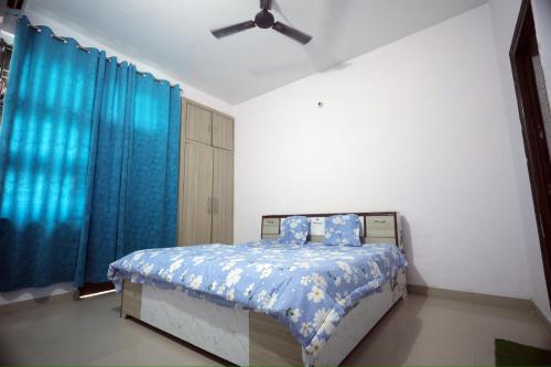a bedroom with a bed with blue curtains and a ceiling fan at Tajiva Stay in Agra