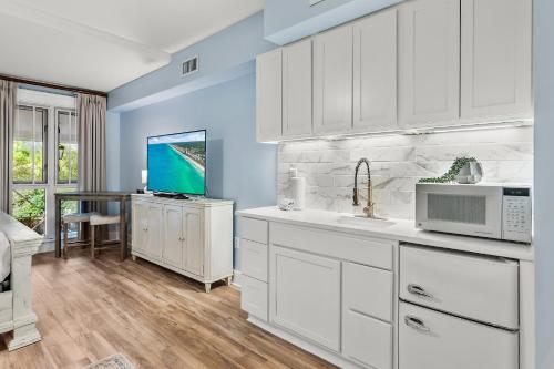 a kitchen with white cabinets and a table with a tv at Grand Sandestin 2210 in Destin