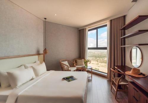 a hotel room with a bed and a desk and a window at Mandala Wins Apec Mũi Né in Mui Ne