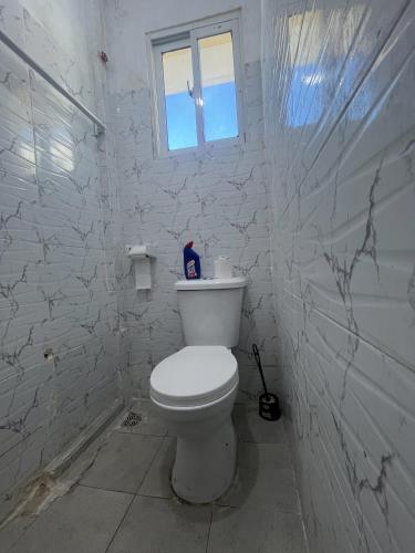 a white bathroom with a toilet and a window at Guest Favorite 1BDR with Washer, Netflix, Parking & Hot Shower 2547,96,065,022 in Mombasa