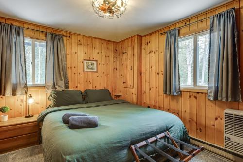 a bedroom with a bed with wooden walls and windows at Riverfront Cabin w/ Hot Tub in Schroon Lake! in Schroon Lake