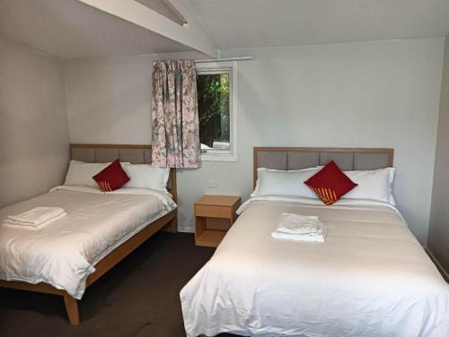 a bedroom with two beds with red pillows and a window at 2 double and 1 sofa beds Chalet D in Rotorua
