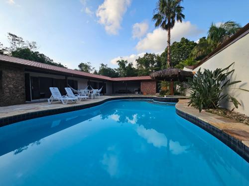 a swimming pool with two chairs and a house at Casa Enorme em condominio, 4 suites, piscina com cascata, cozinha gourmet com churrasueira e fundo com pier no rio para práticas aquaticas in Bertioga