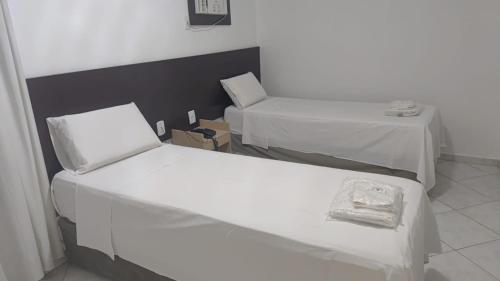 two beds in a room with two tables at Hotel Minas Brasil in Montes Claros