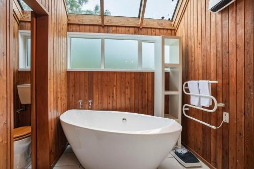 a bathroom with a large white tub and wooden walls at Waitati Retreat in Waitati