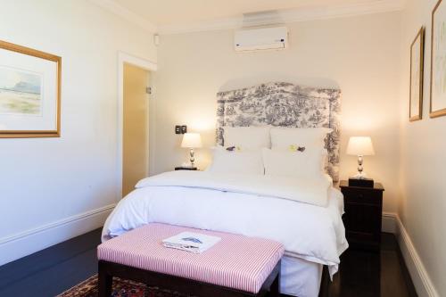 a bedroom with a large white bed and a pink bench at Auberge Daniella in Franschhoek