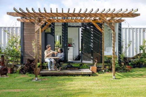 two people sitting at a table under a wooden pergola at Deloraine Tiny Retreat by Tiny Away in Whangarei