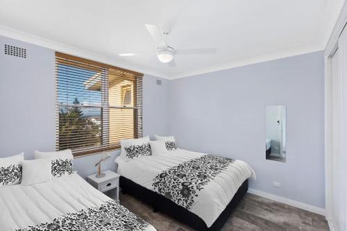 a white bedroom with two beds and a window at Golden Sands Apartment 10 in The Entrance