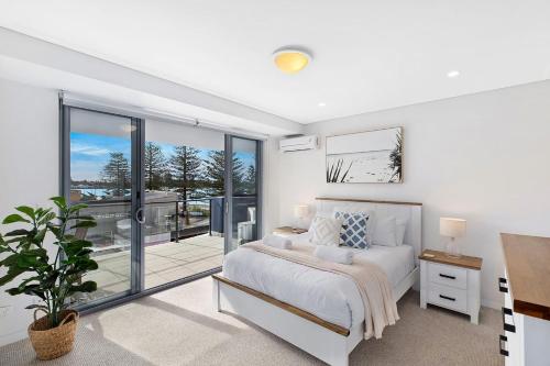 a white bedroom with a bed and a balcony at Coast Apartments 19 Roof Top Pool in The Entrance