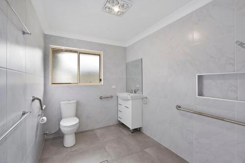 a white bathroom with a toilet and a window at Bonnieview House in Shelly Beach