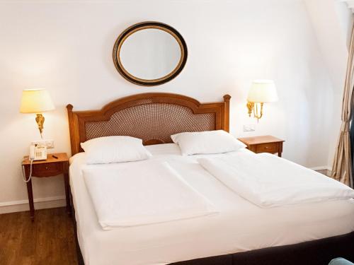 a bedroom with a white bed with a mirror on the wall at DORMERO Hotel Halle in Halle an der Saale