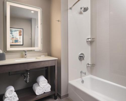 a bathroom with a sink and a tub and a mirror at Hyatt House Schenectady / Mohawk Harbor in Schenectady