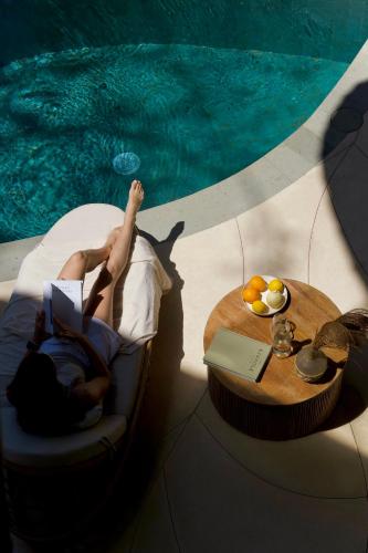 a woman laying in a chair reading a book next to a swimming pool at Cocoon Reserve in Kuta Lombok