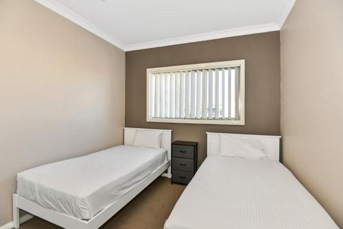 two beds in a small room with a window at The Gallipoli Residence in Long Jetty