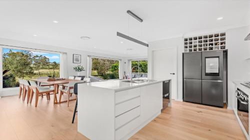 a kitchen with white cabinets and a dining room with a table at 21 Forever in Pokolbin