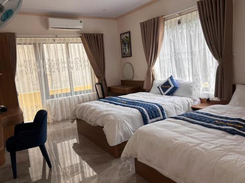a bedroom with two beds and a chair and windows at Long Bình Hotel in Dong Hoi
