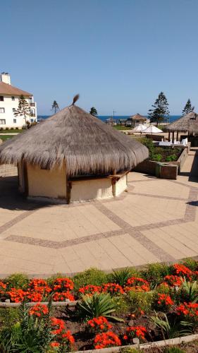 a hut with a grass roof and some flowers at A Pasos de la Playa in Papudo