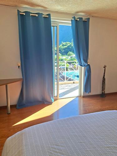 a bedroom with a bed and a window with blue curtains at Villa Dijoux D'O in Entre-Deux