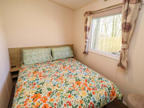 a bedroom with a bed with a floral comforter and a window at Sunflower Retreat, Caravan 61 in Morpeth